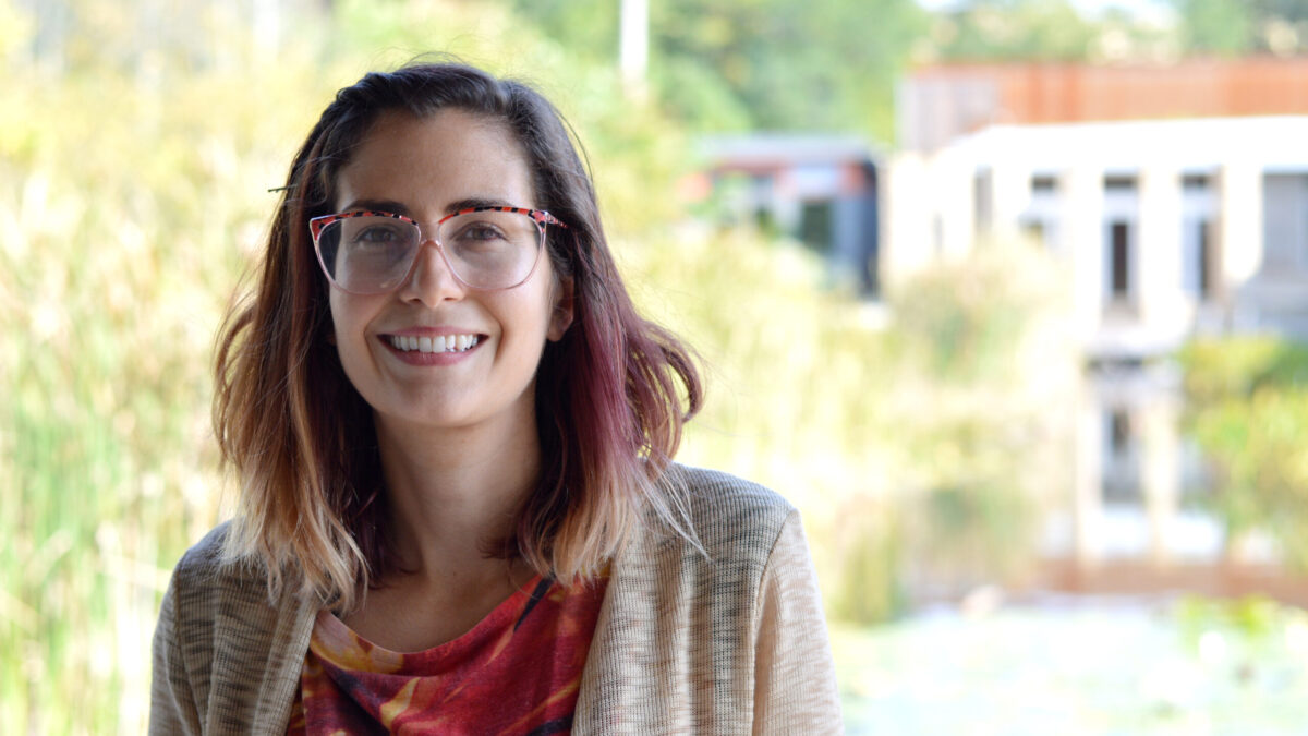 Adult with long dark red hair and glasses smiling in profile