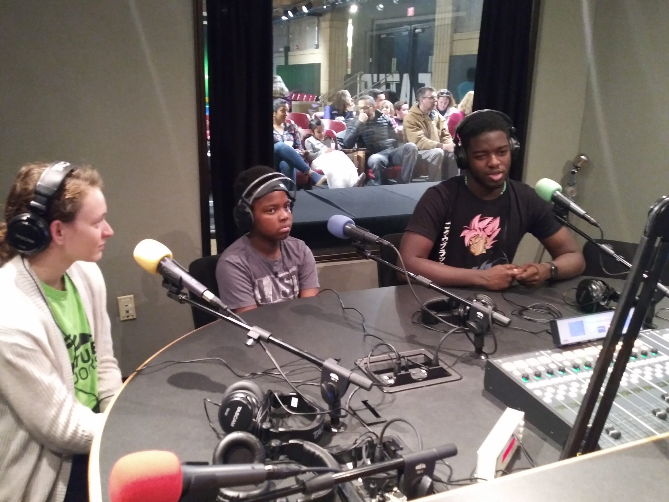 Three youth wearing headphones sitting in front of microphones in a radio studio
