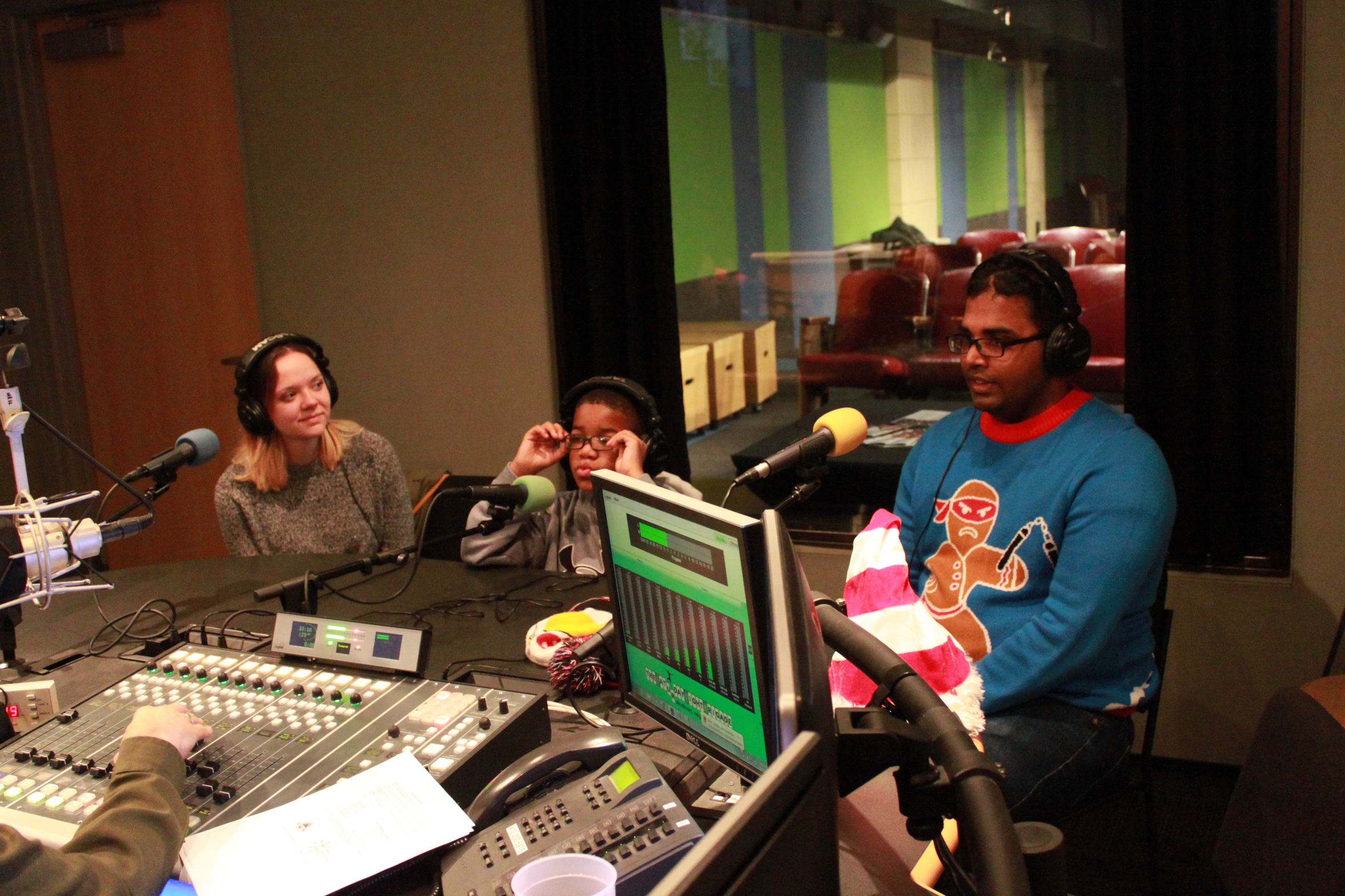 Three youth wearing headphones and speaking into microphones being interviewed in a radio studio