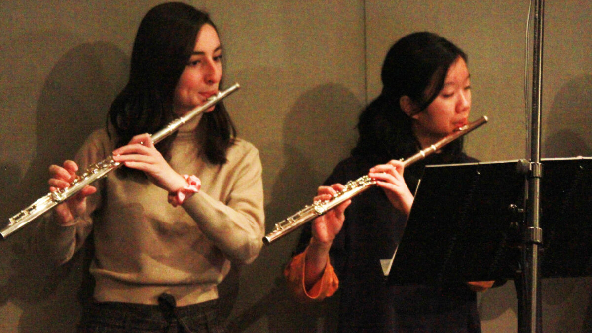Two teens playing flutes and looking at a music stand in a radio studio