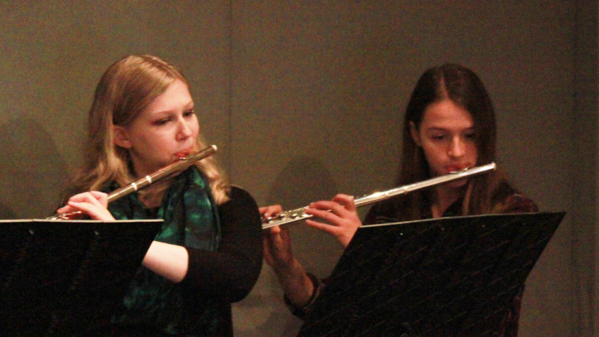 Two teens playing flute and looking at music stands in a radio studio