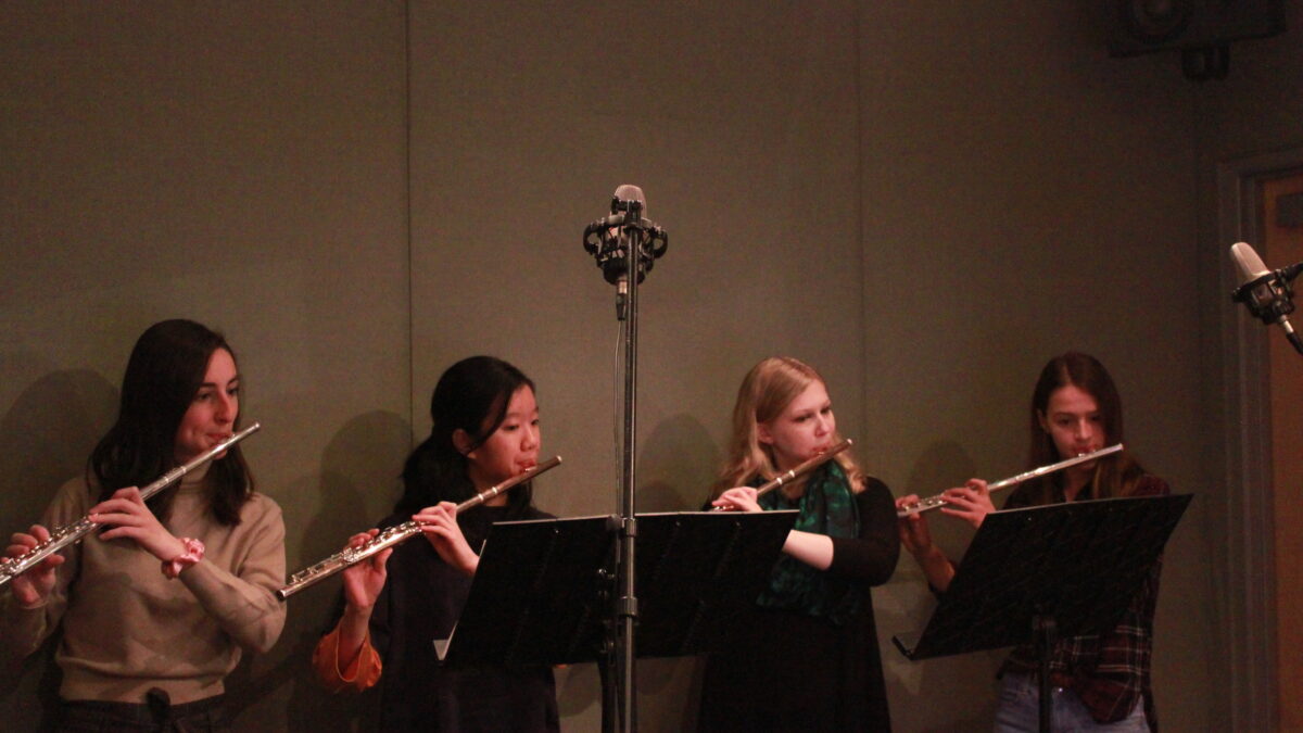 Four teens playing flute and looking at music stands in a radio studio