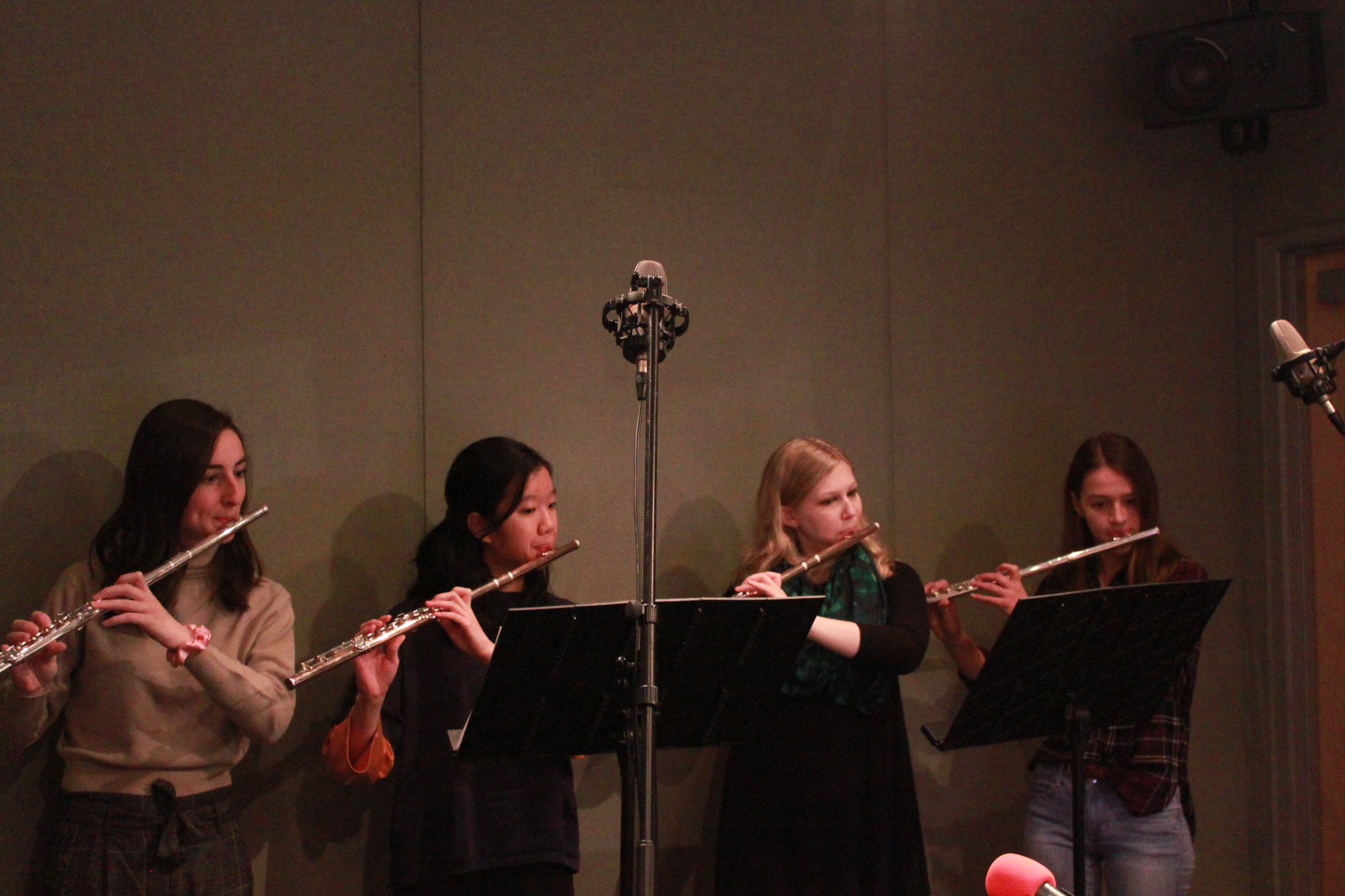 Four teens playing flute and looking at music stands in a radio studio