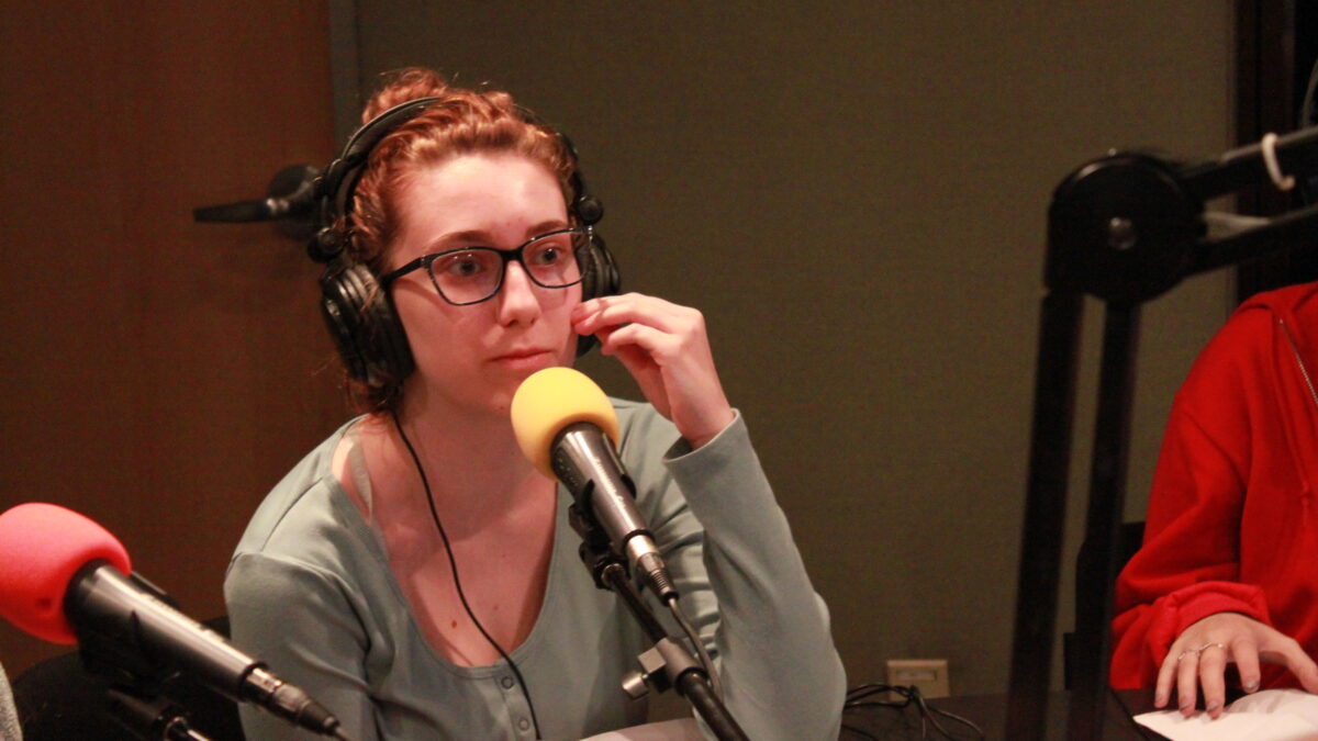 Teen wearing glasses and headphones speaking into a microphone in a radio studio