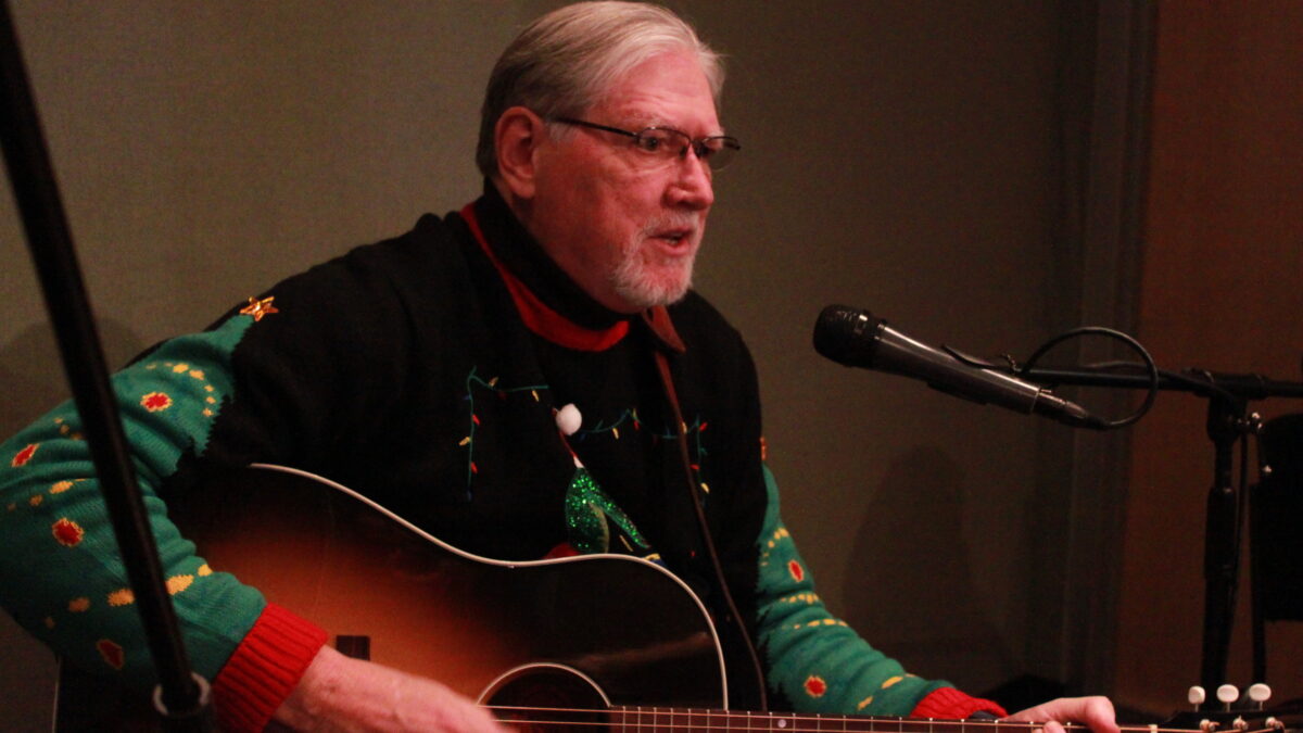 Adult playing guitar and singing into a microphone in a radio studio