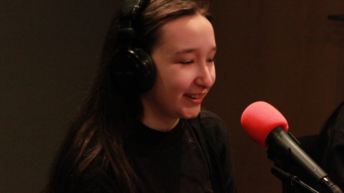 Teen wearing headphones speaking into a microphone in a radio studio