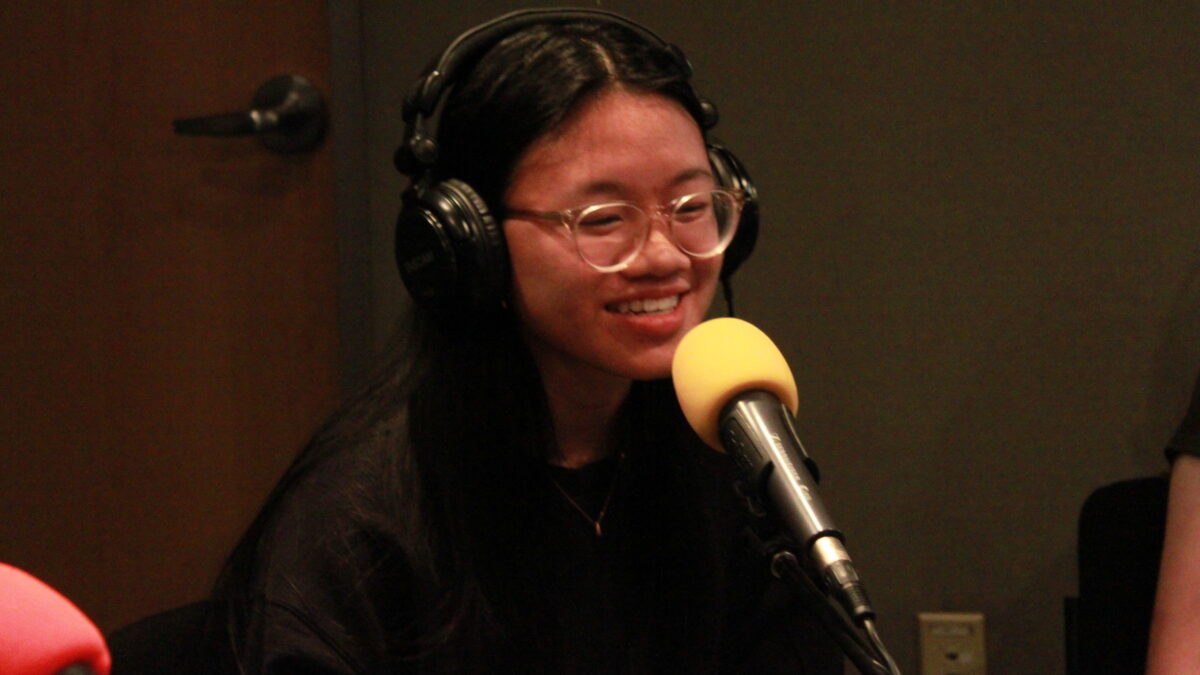 Teen wearing glasses and headphones speaking into a microphone in a radio studio