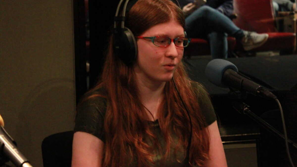 Teen wearing headphones and glasses speaking into a microphone in a radio studio