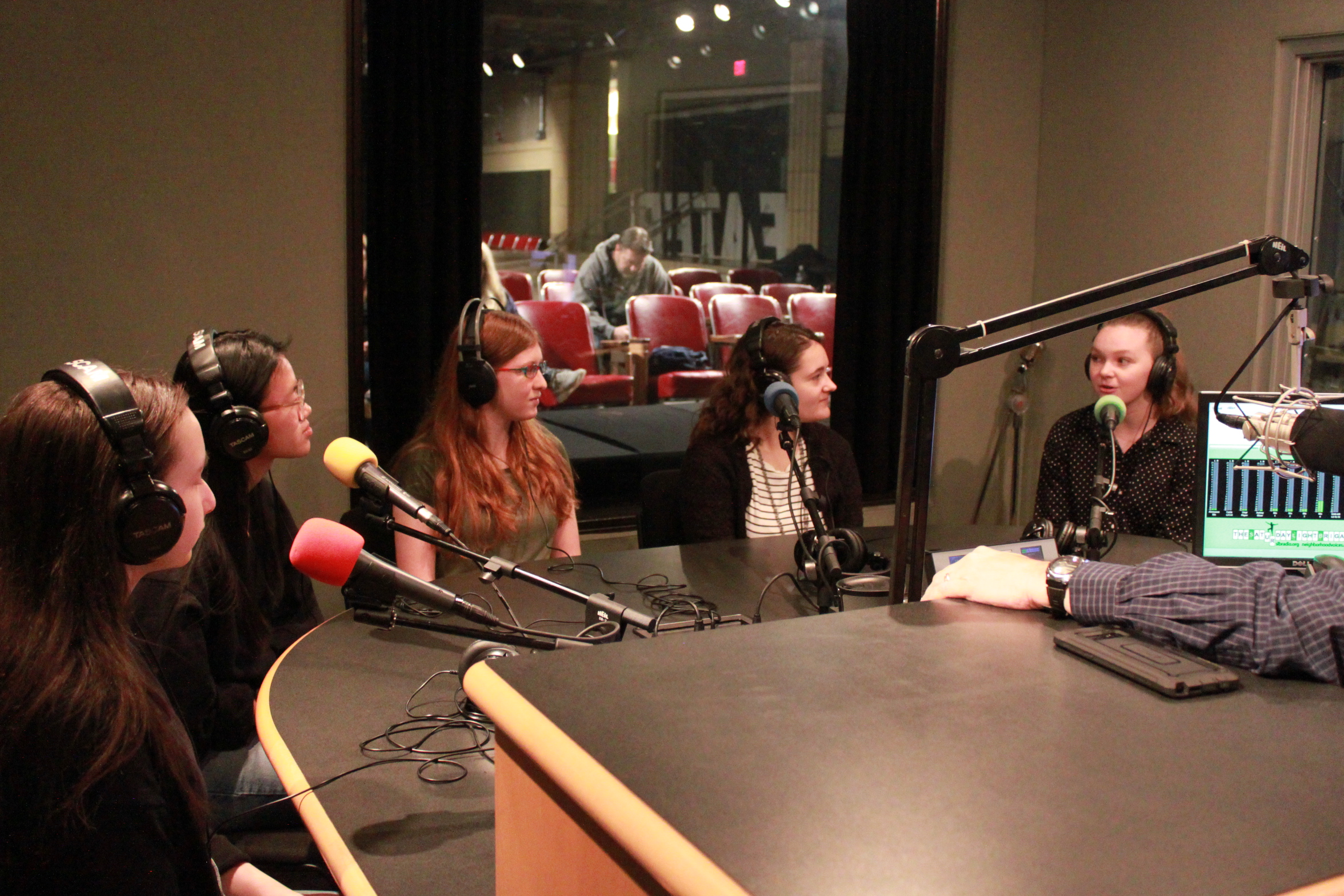 Five teens wearing headphones and speaking into microphones in a radio studio