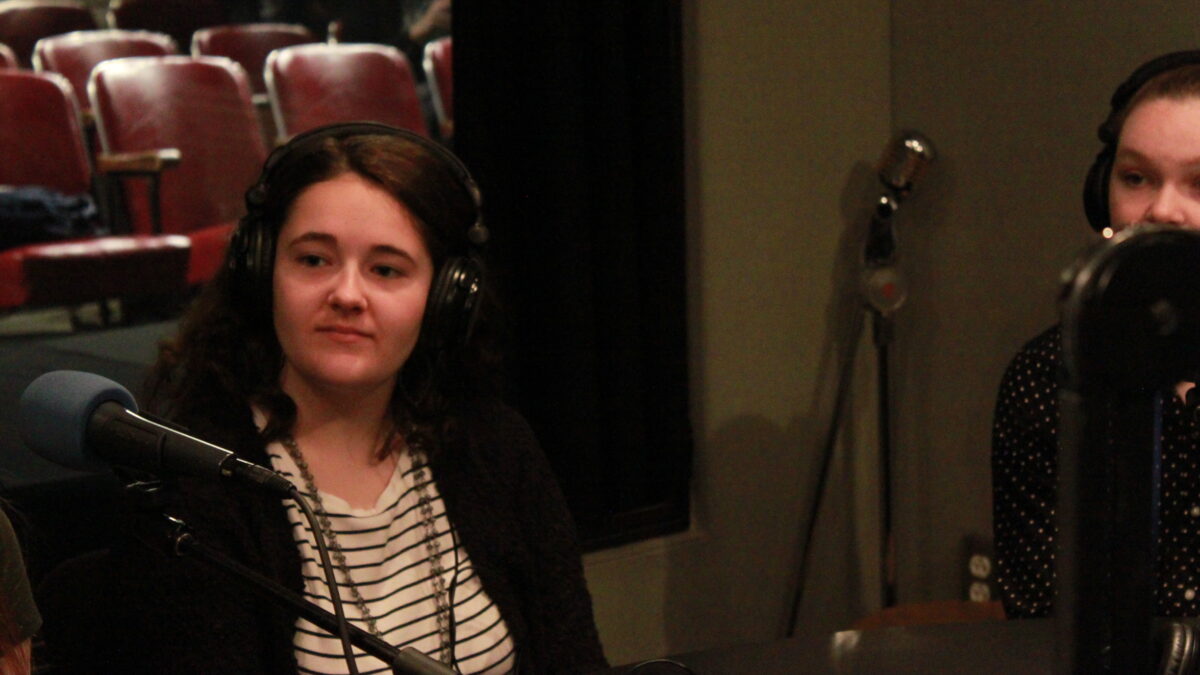Two teens wearing headphones sitting in front of microphones in a radio studio