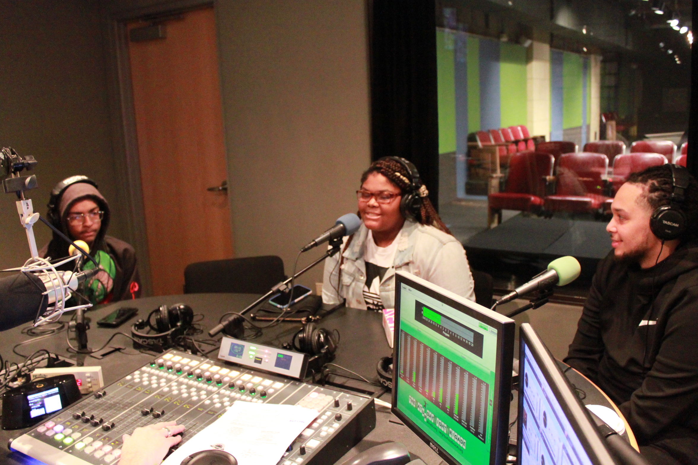 Three teens wearing headphones and speaking into microphones in a radio studio