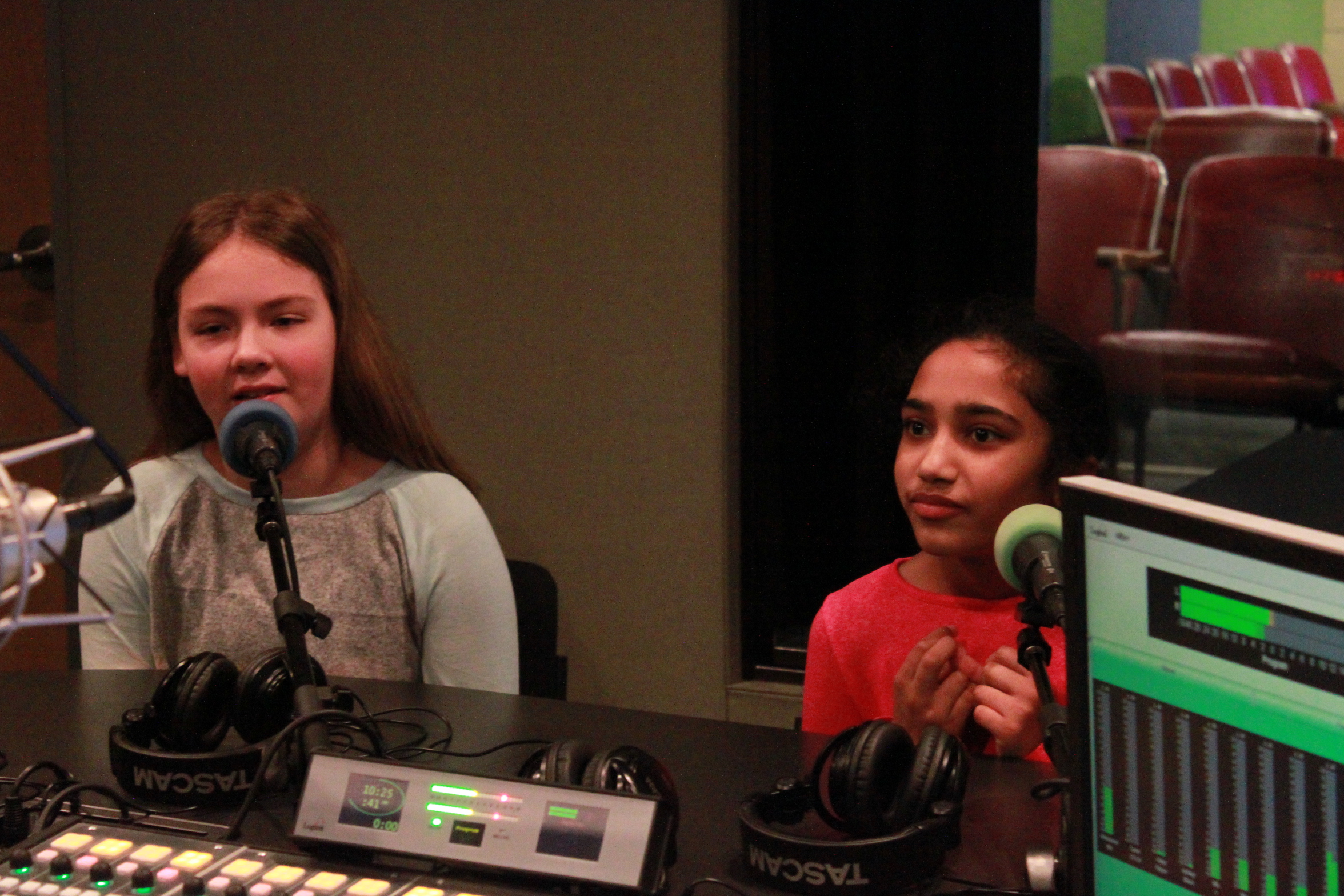 Two children speaking into microphones in a radio studio