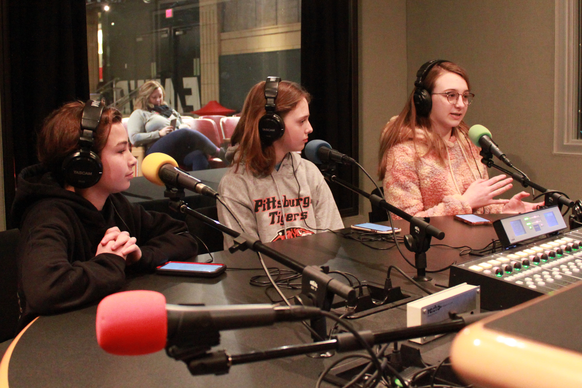 Three youth wearing headphones and speaking into microphones in a radio studio
