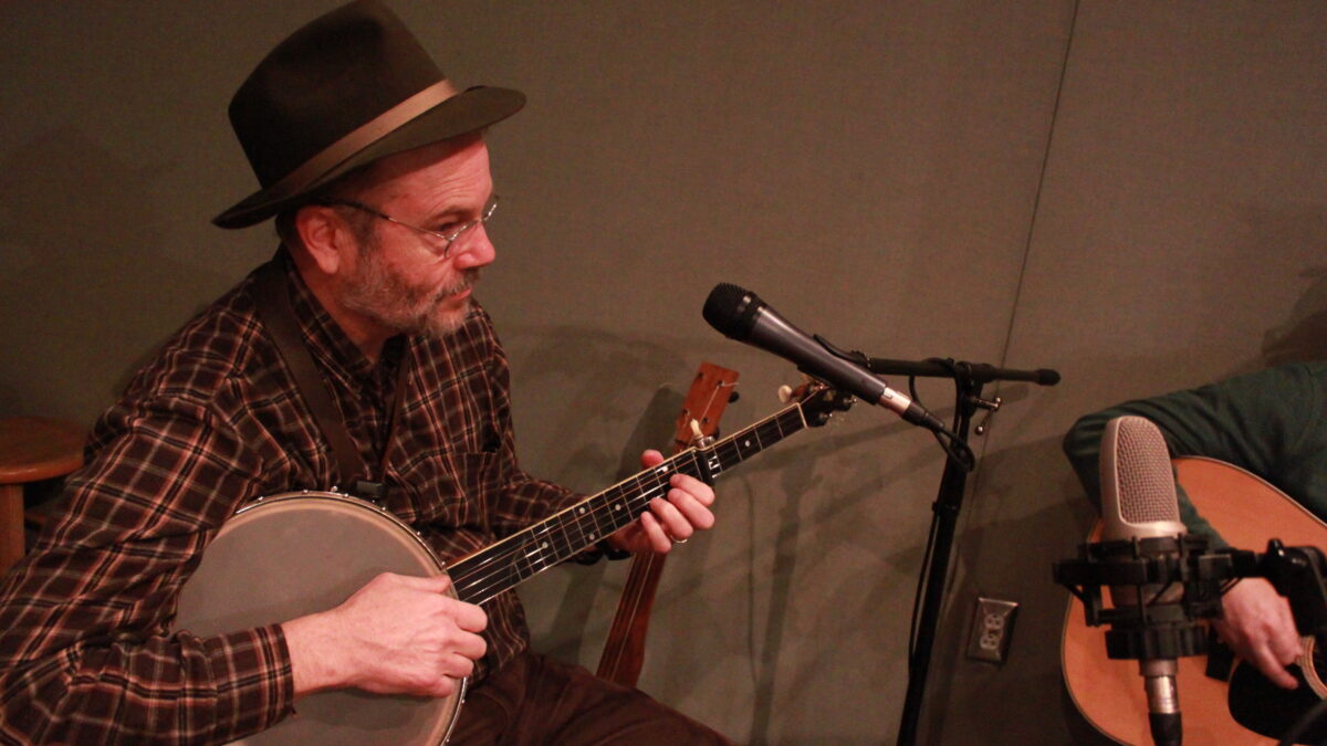 Adult playing banjo in front of a microphone in a radio studio