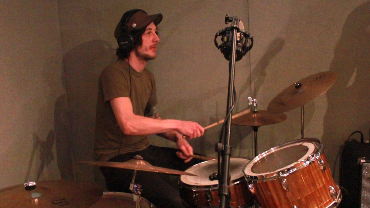 Adult wearing headphones playing on a drum set in a radio studio