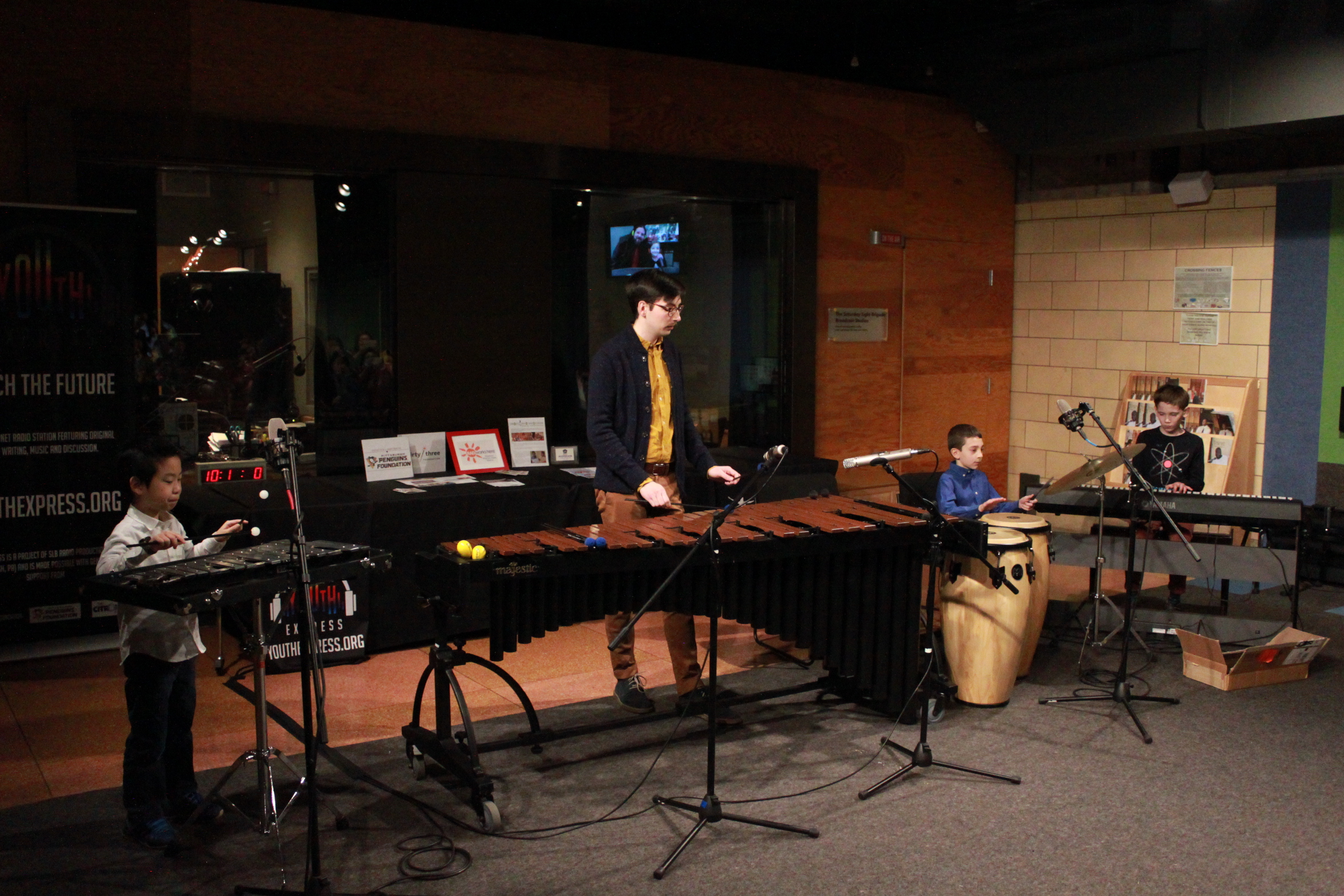 Three youth and one adult performing on glockenspiel, xylophone, congas, and piano keyboard