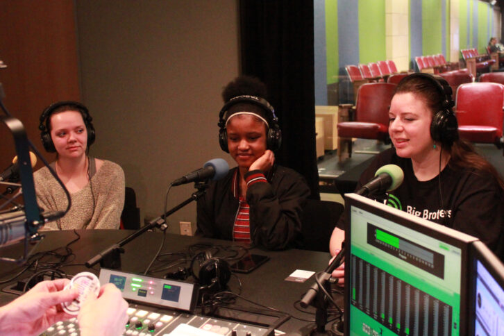 Two youth and an adult. all wearing headphones being interviewed in a radio studio