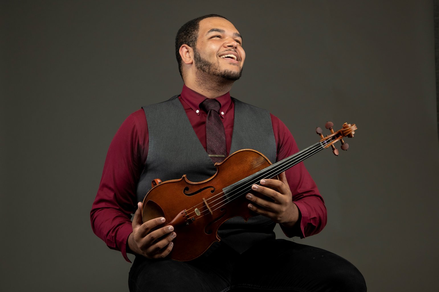 An adult smiling in profile while holding a violin
