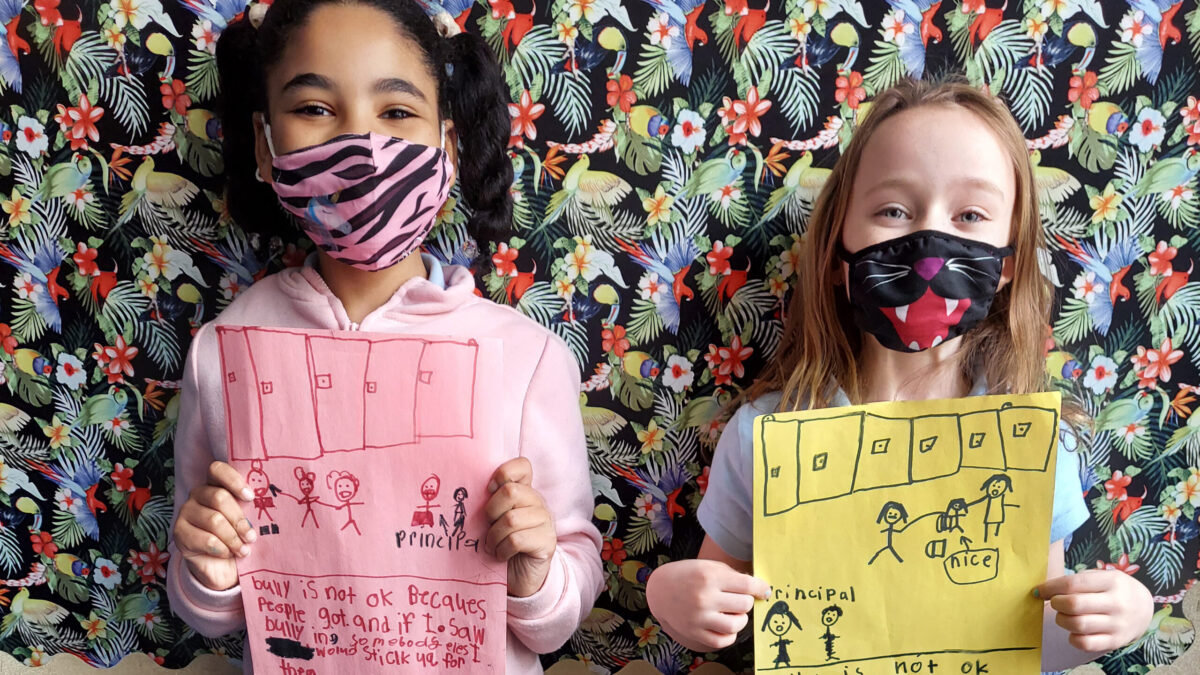 Two children holding papers with drawings of bullying occurring, and text explaining why bullying is wrong