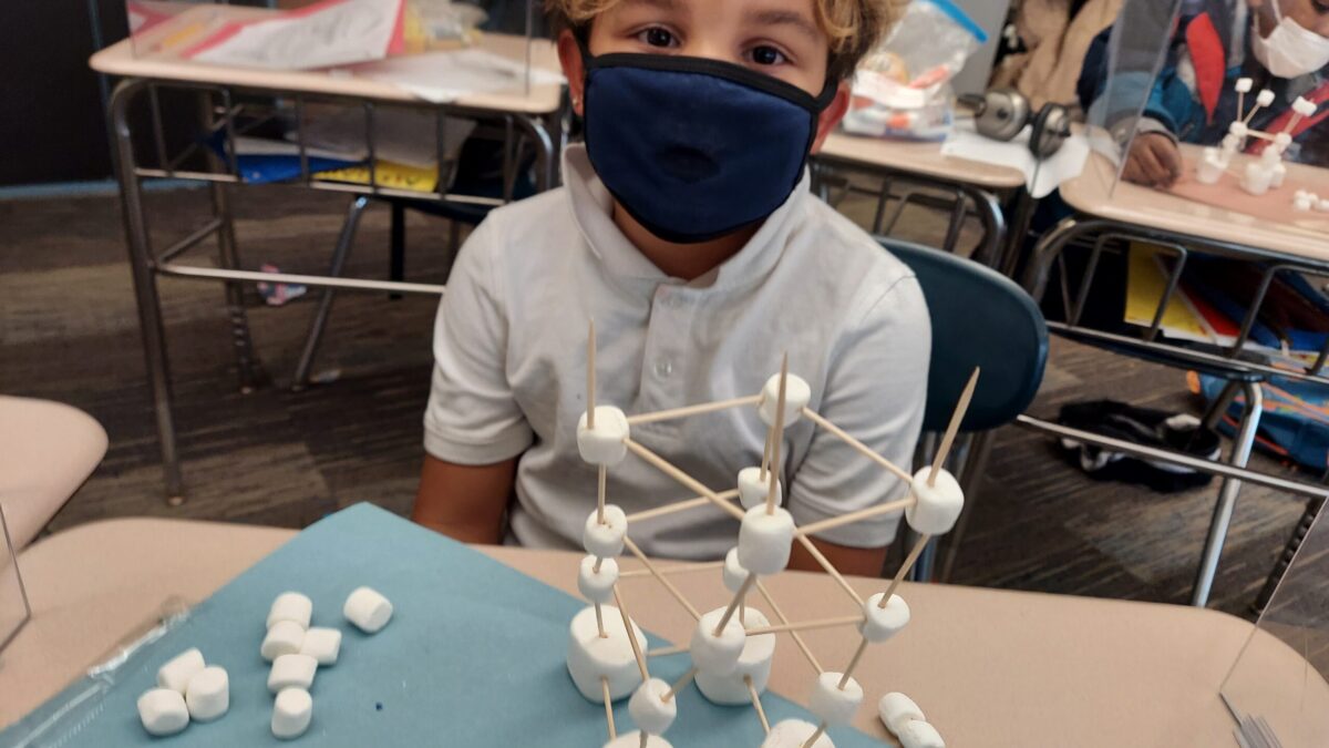 A child sitting in front of a structure built out of toothpicks and marshmallows
