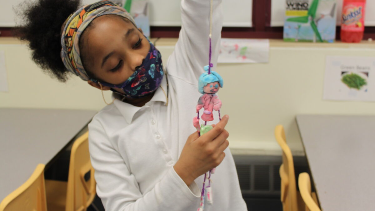 A child holding a sculpture of an individual made out of clay and strings