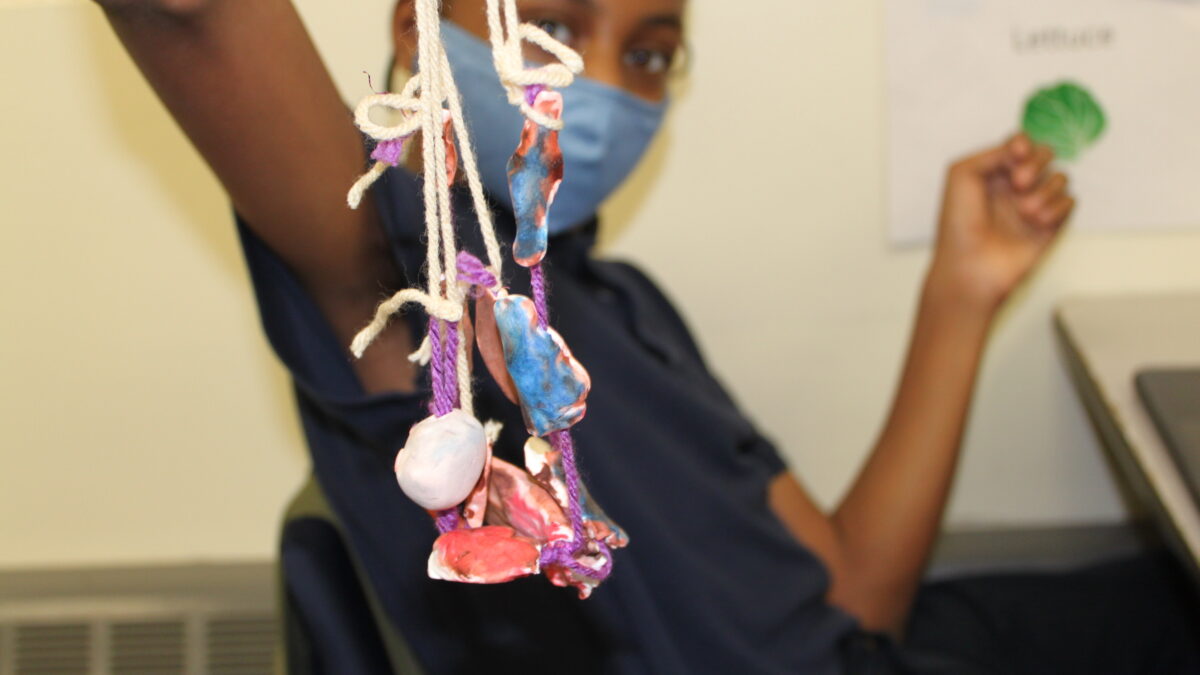 A child holding a sculpture of an individual made out of clay and strings