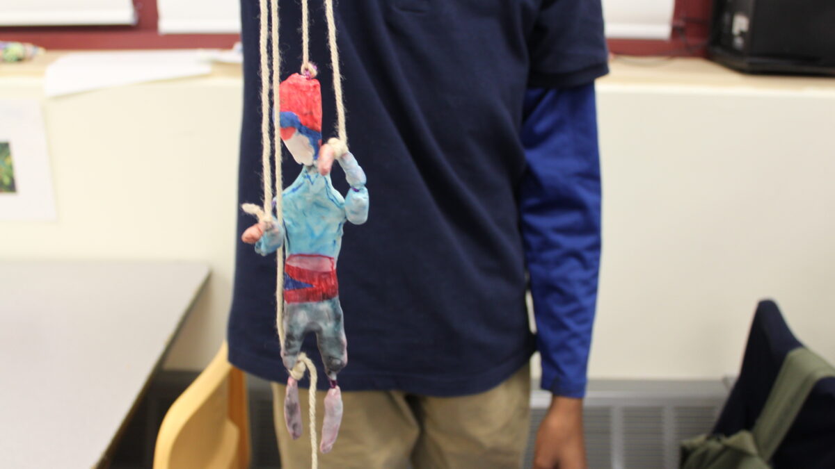 A person holding a sculpture of an individual made of clay and strings