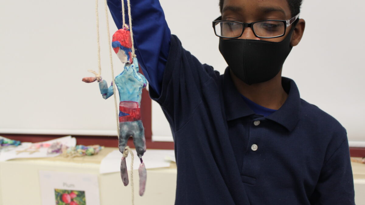A child holding a sculpture of an individual made out of clay and strings