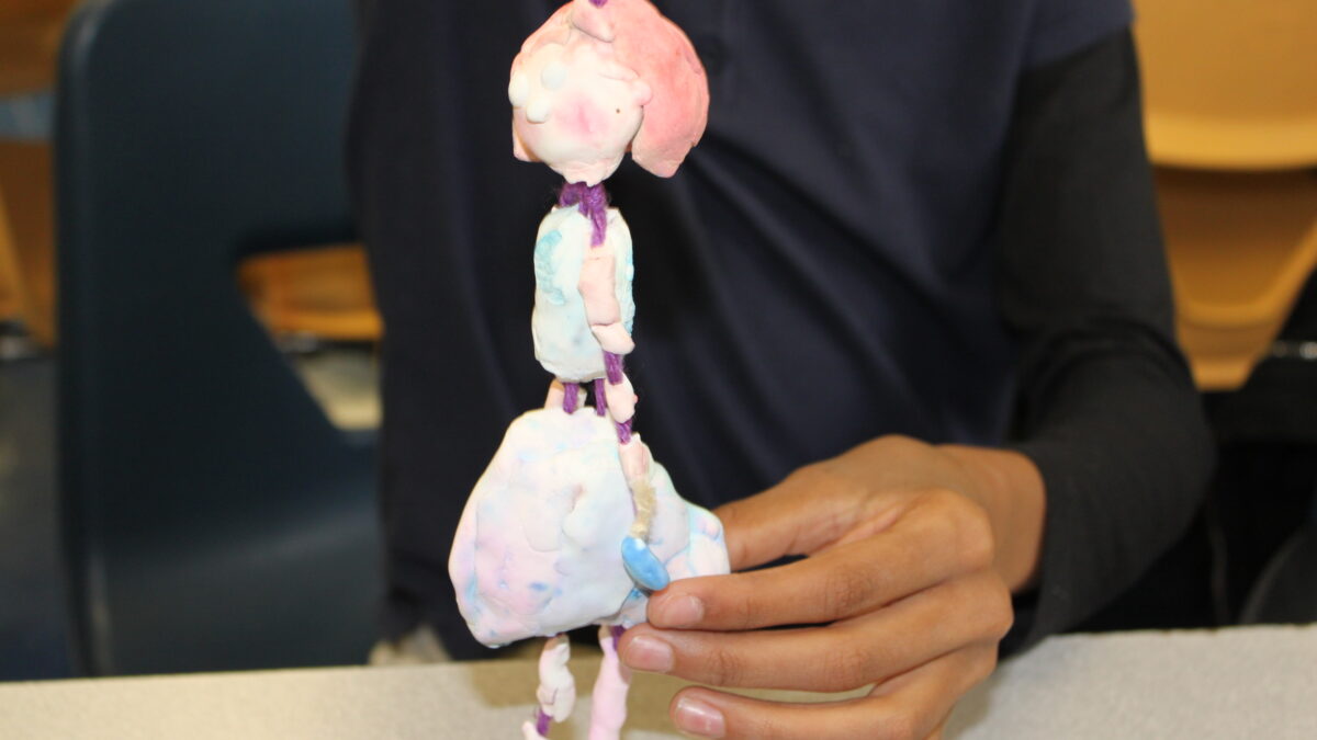 A hand holding a clay sculpture of an individual held together by string