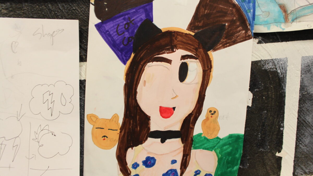 A drawing of an individual with cat ears, long brown hair, and a collar winking and smiling, with dogs and cats in the background