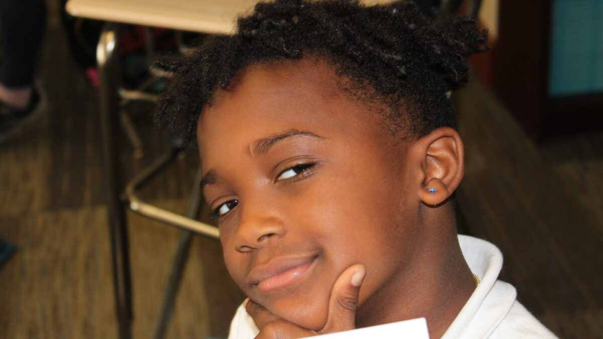 A child with short curly black hair smirking and posing in profile