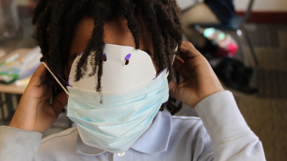 A child hiding their face by sticking a paper mask inside their face mask