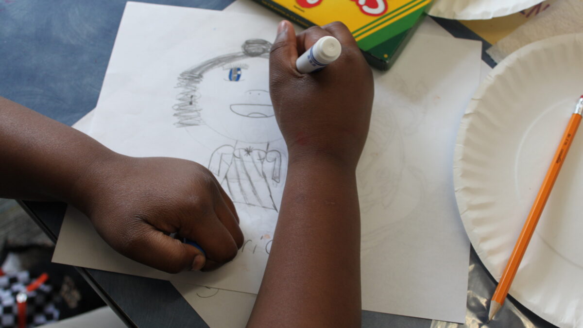A child using a marker to add the color blue to the eyes of a drawing of an individual