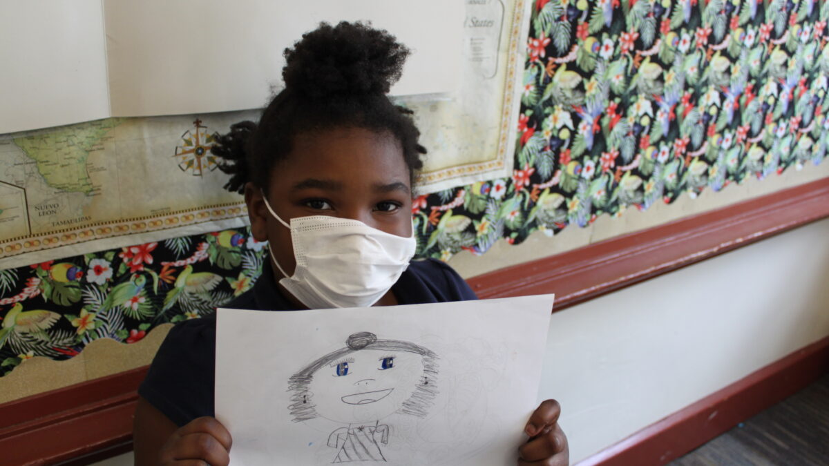 A child holding a drawing of an individual with their hair in a bun and a dress, with the text "Lyric" written underneath