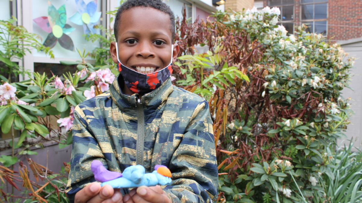 A child holding a light blue clay creature in a garden