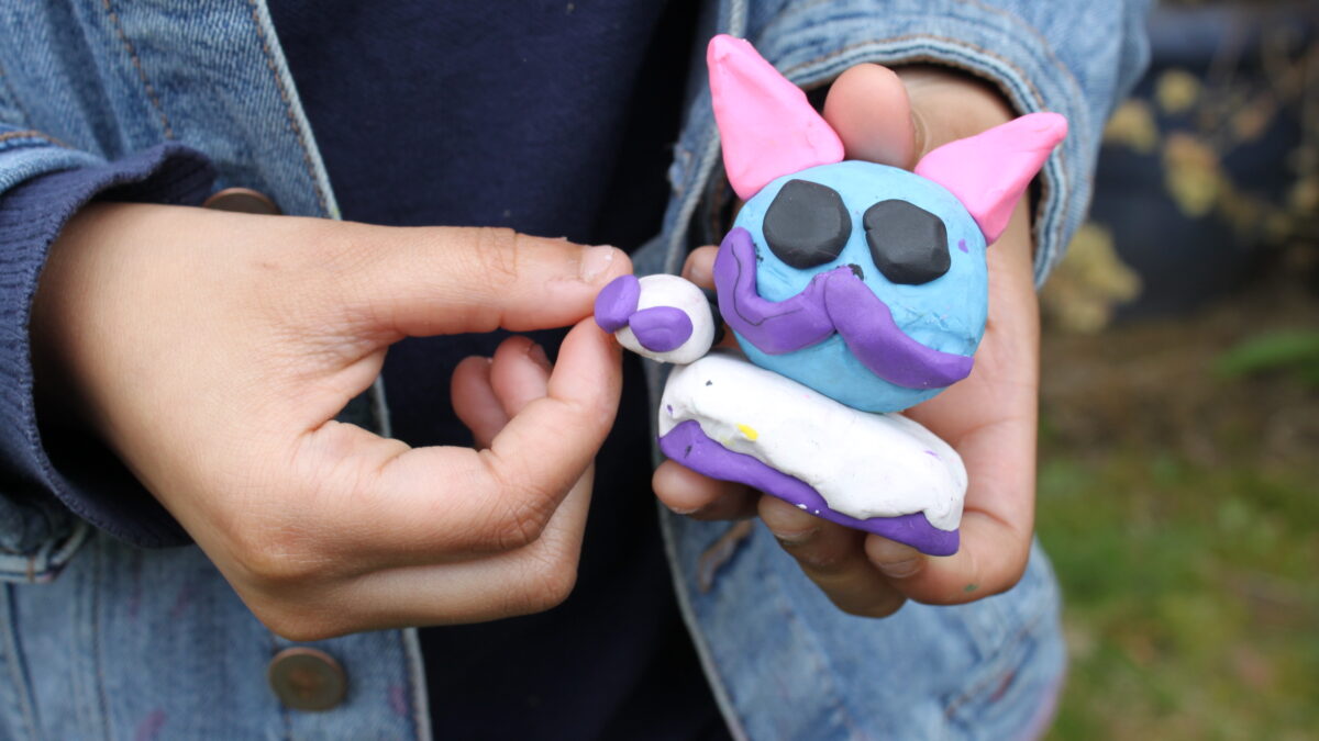A person holding a blue clay object shaped like a cat's head
