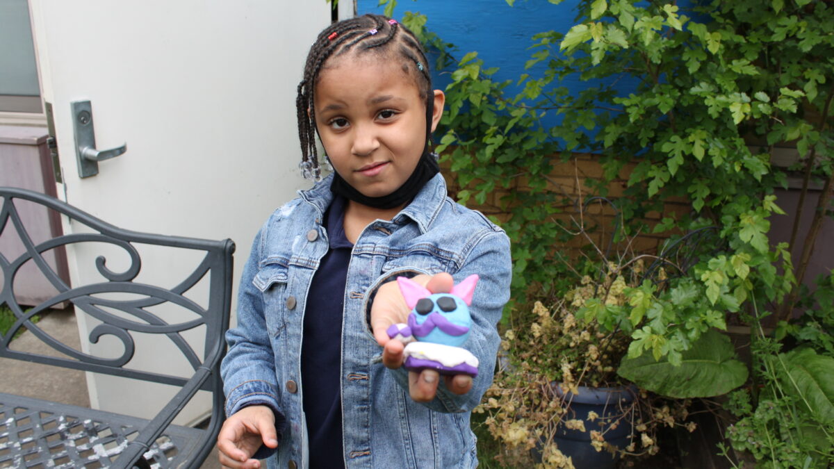 A child holding a blue clay object shaped like a cat's head in a garden