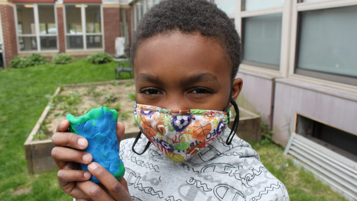 A child holding a green and blue clay cup shaped object in a garden