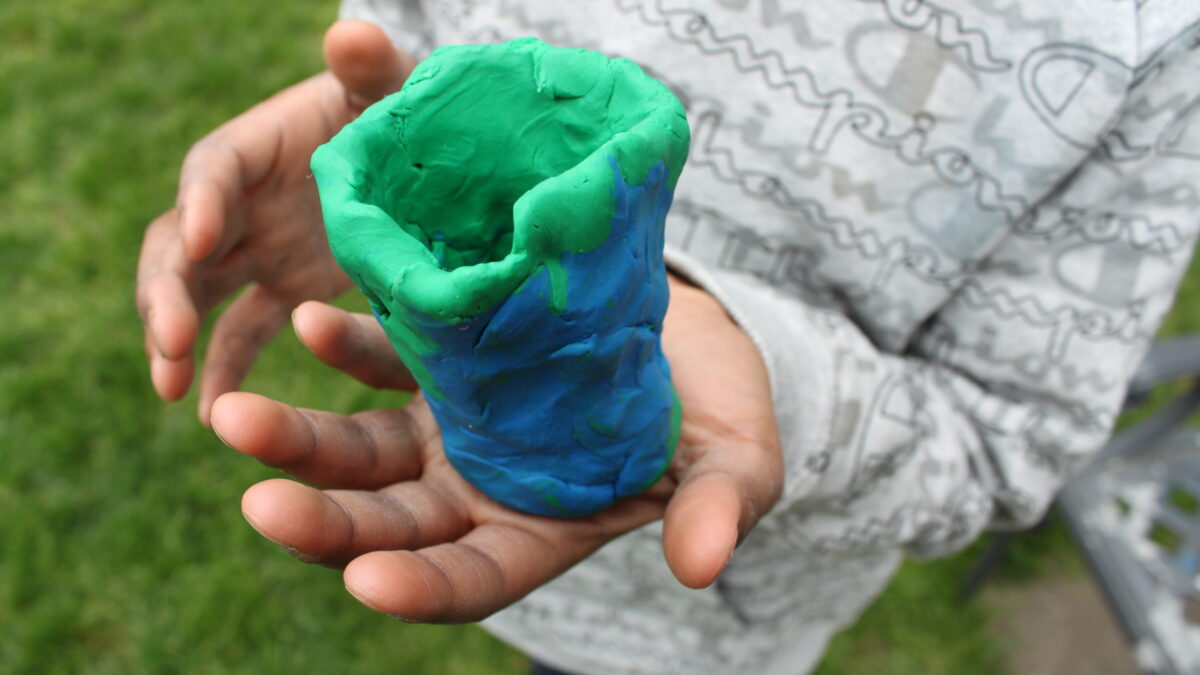 A person holding a green and blue clay cup shaped object in a garden