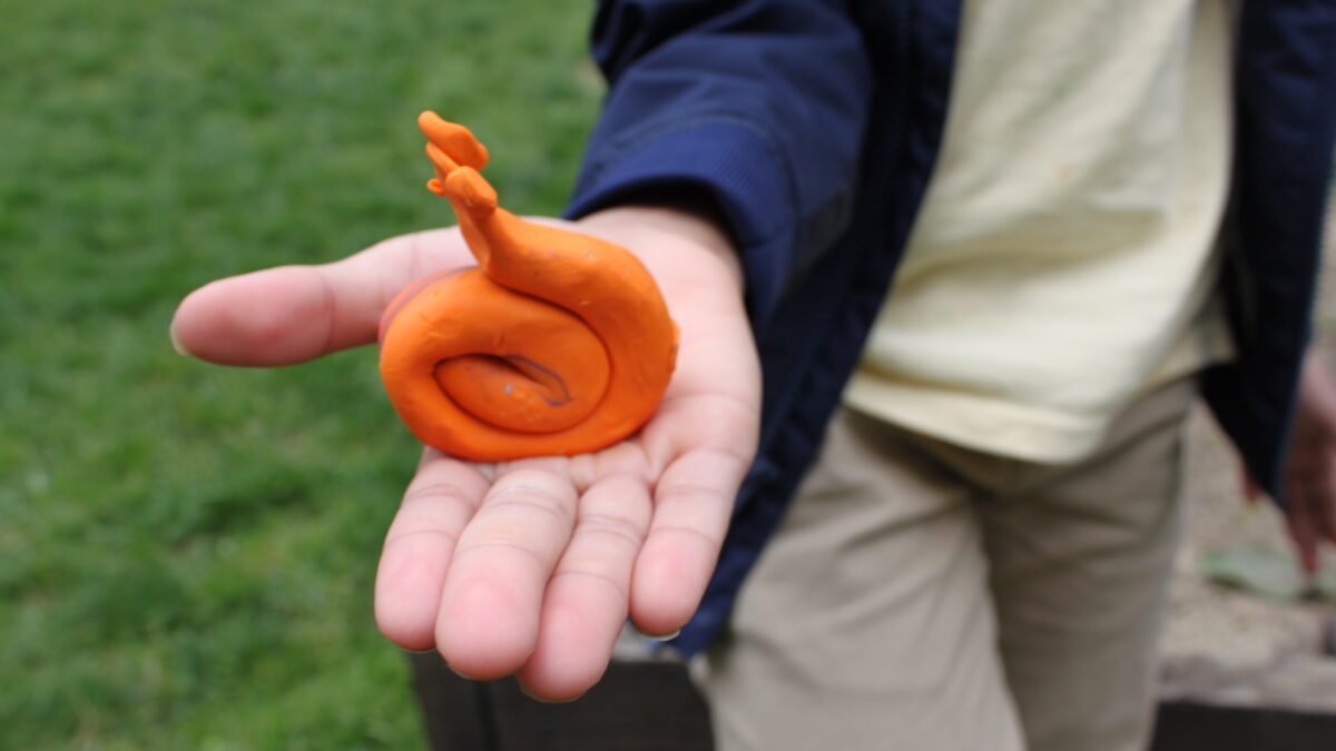 A person holding an orange clay snail creature in a garden
