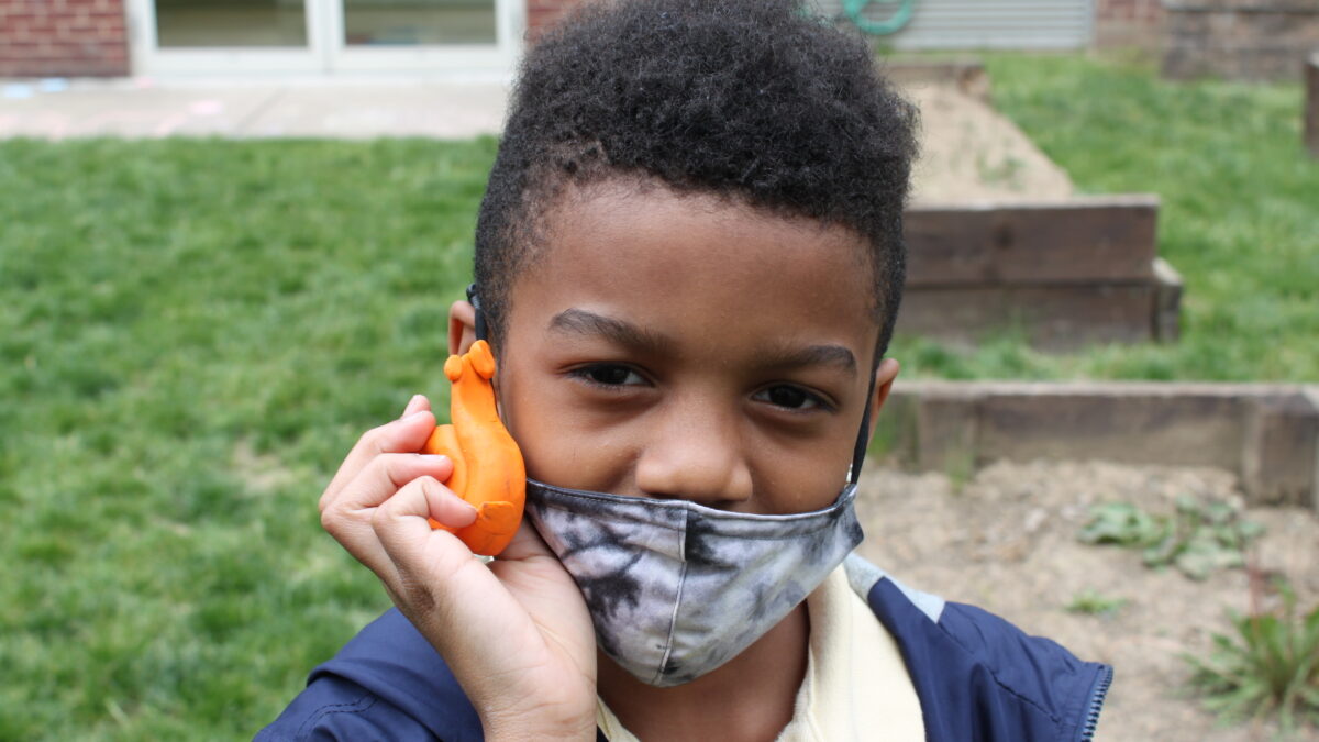 A child holding an orange clay snail creature in a garden