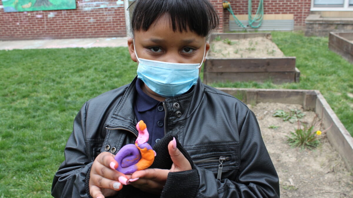 Youth in a black leather jacket holding a purple and orange clay snail creature in a garden