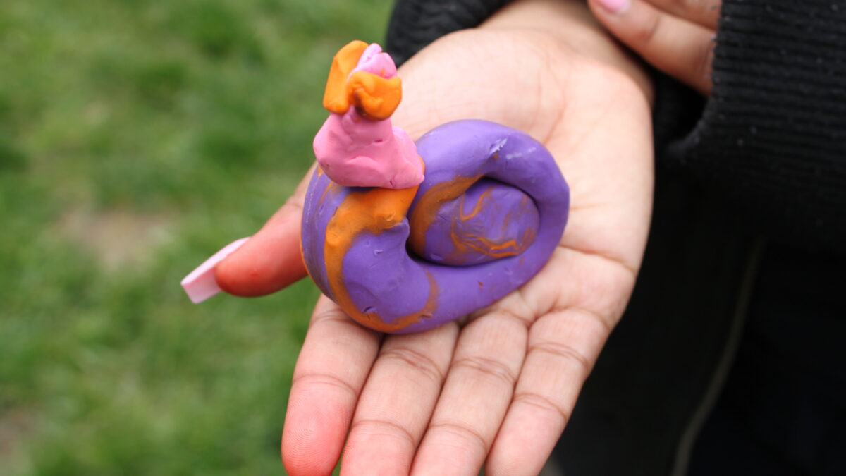 A person holding a purple and orange clay snail creature