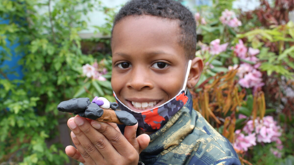 A child holding a black clay creature in a garden