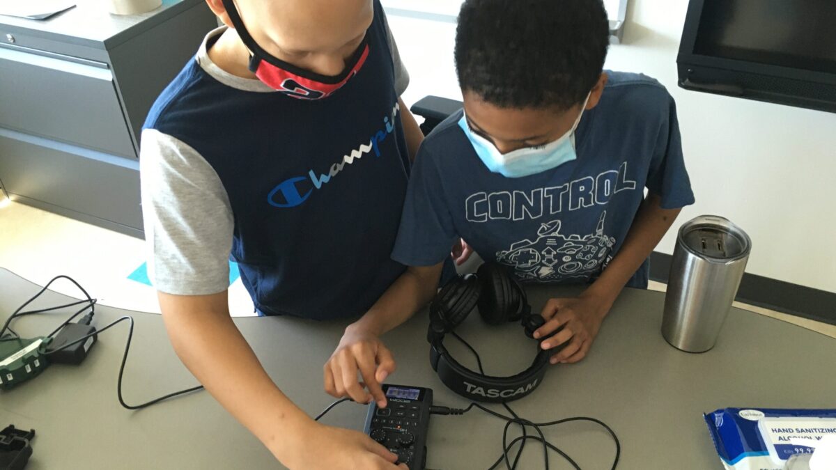 Two youth wearing face masks interacting with a portable recorder on a table