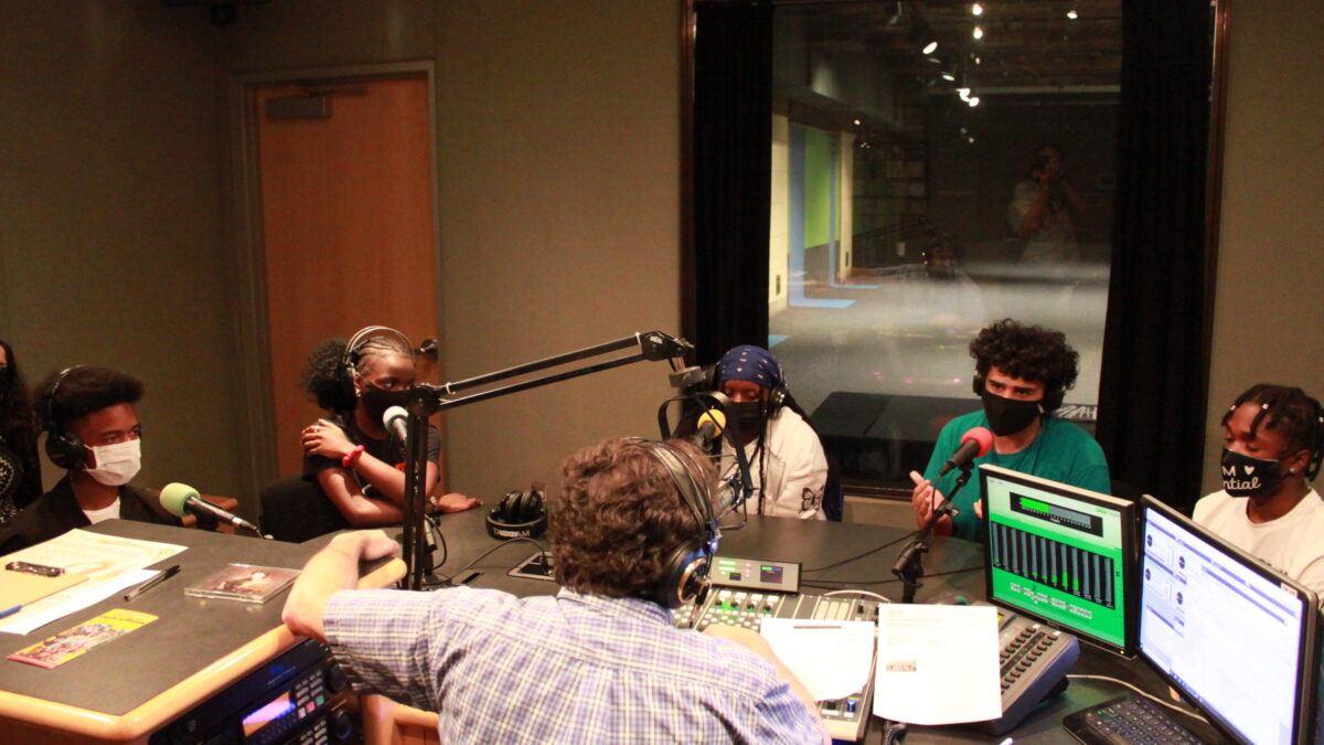 Five youth wearing headphones and face masks being interviewed in a radio studio