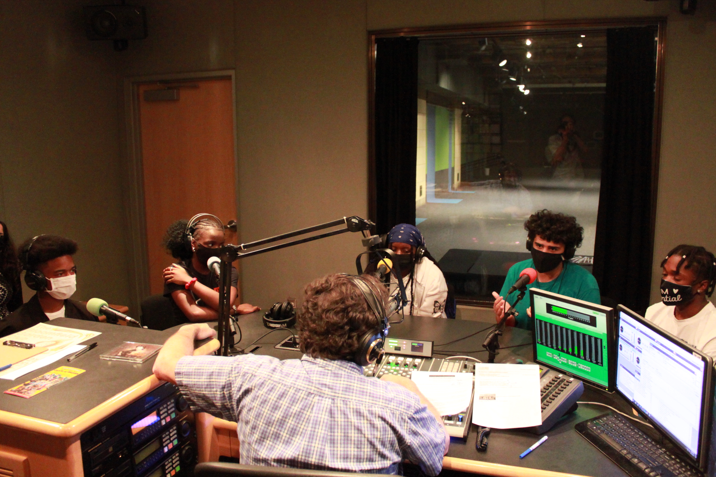 Five youth wearing headphones and face masks being interviewed in a radio studio