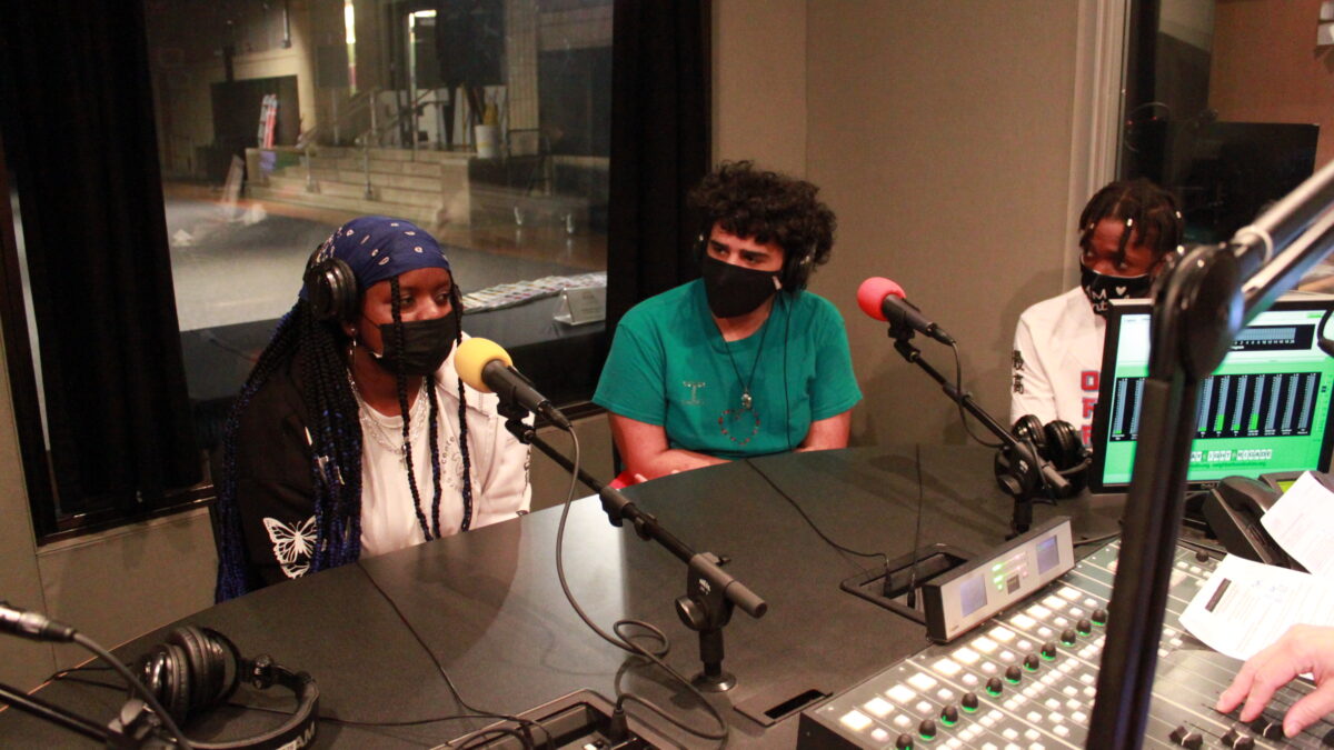 Three youth wearing face masks and headphones being interviewed in a radio studio