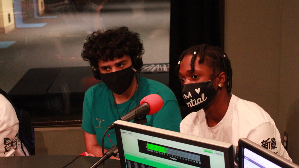 Two youth wearing face masks, one wearing headphones, being interviewed in a radio studio