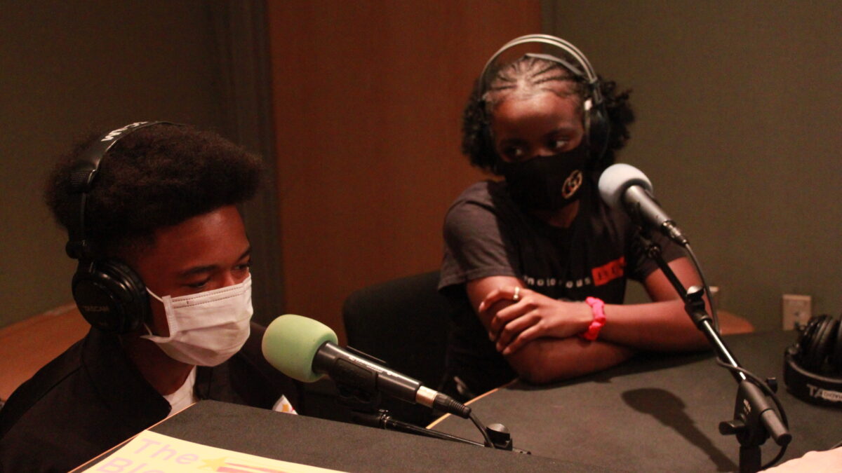 Two youth wearing headphones and face masks being interviewed in a radio studio